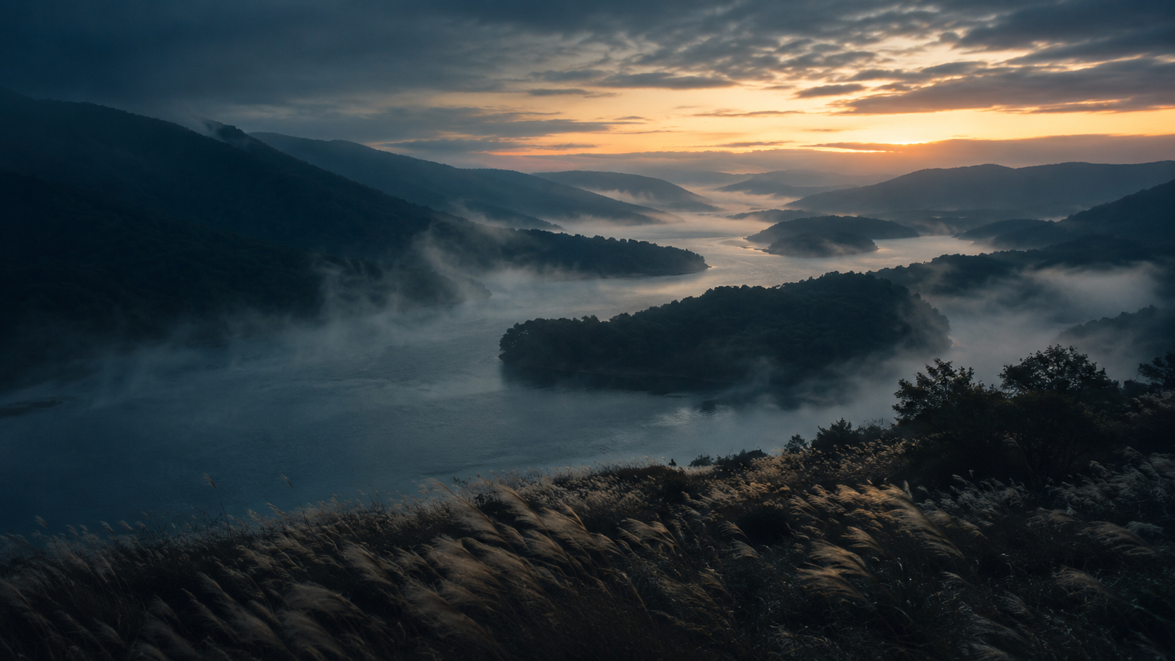 Mist moving through a dark river valley at dawn